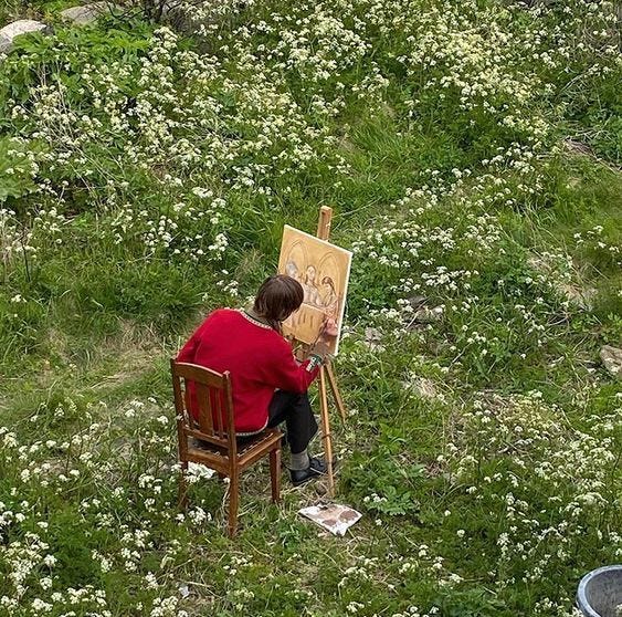 This may contain: a person sitting in a chair painting on an easel