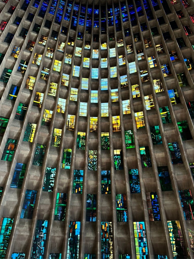 Interior of modernist concrete wall with colourful rectangular stained glass windows.