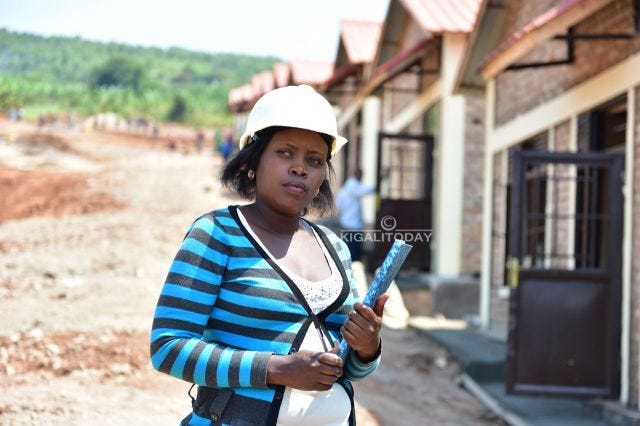 Photo of Bihoyiki Valantine, a Rwandan woman holding a blueprint and wearing a hard hat in front of construction that she's overseeing
