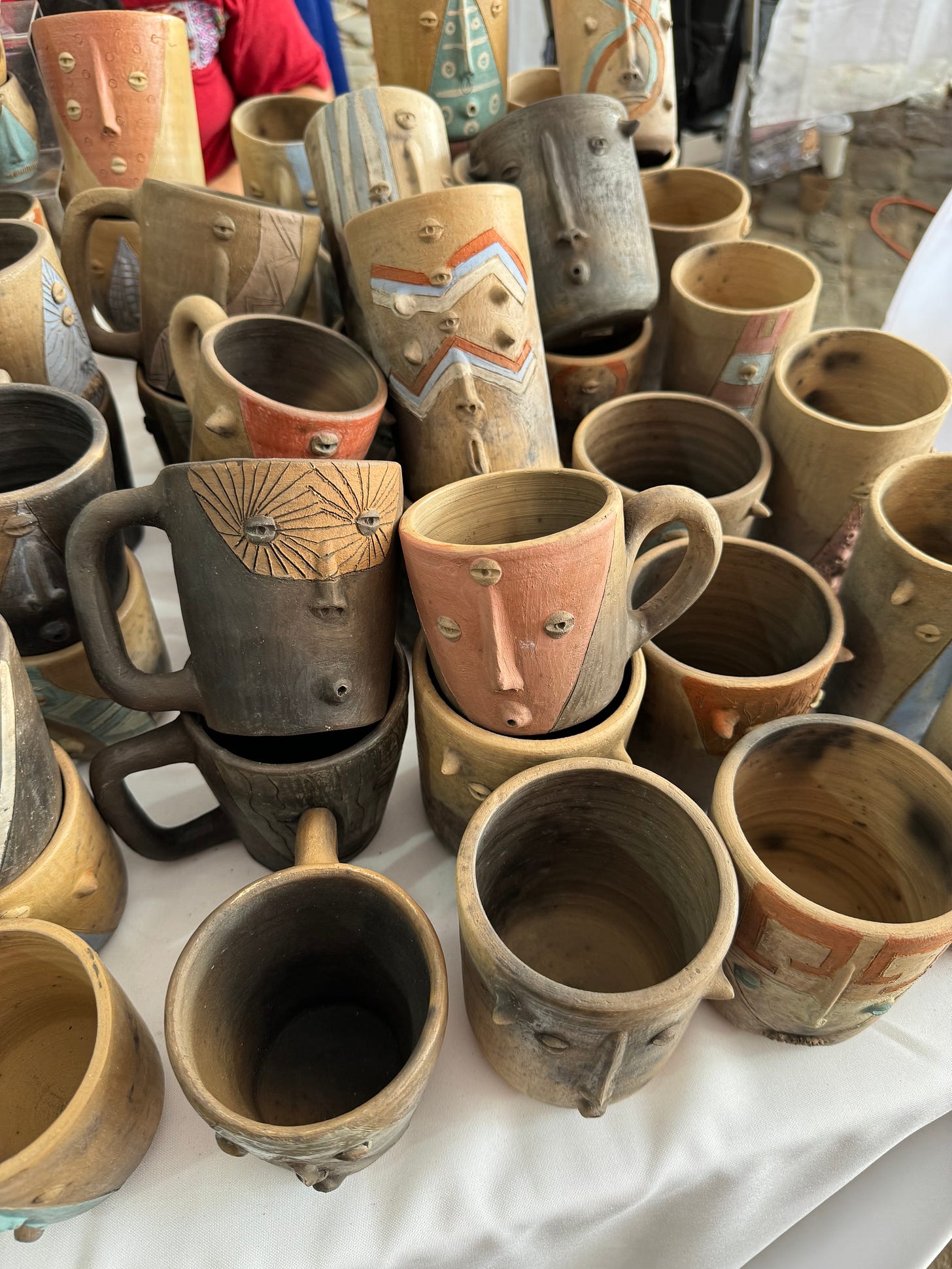 A number of mugs and plant pots with designs and faces on them sitting on a table.