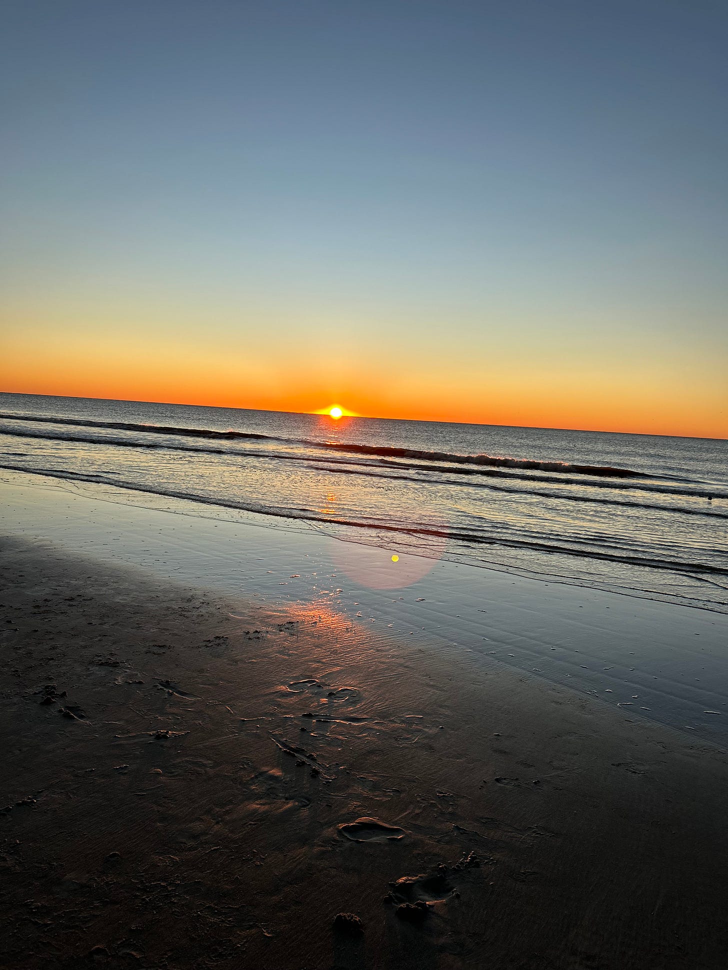 An orange and yellow hued sunrise over the waves of the beach