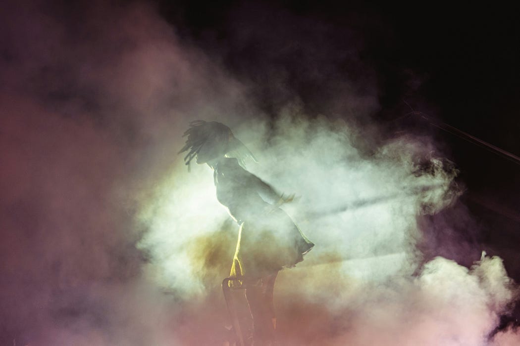 a woman on a dark stage, alone. clouds of light and smoke surround her.