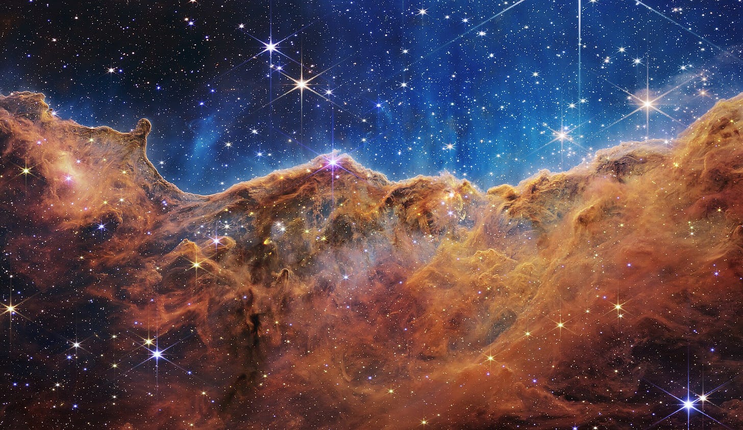 English: What looks much like craggy mountains on a moonlit evening is actually the edge of a nearby, young, star-forming region NGC 3324 in the Carina Nebula. Captured in infrared light by the Near-Infrared Camera (NIRCam) on NASA’s James Webb Space Telescope, this image reveals previously obscured areas of star birth.  Called the Cosmic Cliffs, the region is actually the edge of a gigantic, gaseous cavity within NGC 3324, roughly 7,600 light-years away. The cavernous area has been carved from the nebula by the intense ultraviolet radiation and stellar winds from extremely massive, hot, young stars located in the center of the bubble, above the area shown in this image. The high-energy radiation from these stars is sculpting the nebula’s wall by slowly eroding it away.  NIRCam – with its crisp resolution and unparalleled sensitivity – unveils hundreds of previously hidden stars, and even numerous background galaxies. Several prominent features in this image are described below.  -- The “steam” that appears to rise from the celestial “mountains” is actually hot, ionized gas and hot dust streaming away from the nebula due to intense, ultraviolet radiation.  -- Dramatic pillars rise above the glowing wall of gas, resisting the blistering ultraviolet radiation from the young stars.  -- Bubbles and cavities are being blown by the intense radiation and stellar winds of newborn stars.  -- Protostellar jets and outflows, which appear in gold, shoot from dust-enshrouded, nascent stars.  -- A “blow-out” erupts at the top-center of the ridge, spewing gas and dust into the interstellar medium.  -- An unusual “arch” appears, looking like a bent-over cylinder.  This period of very early star formation is difficult to capture because, for an individual star, it lasts only about 50,000 to 100,000 years – but Webb’s extreme sensitivity and exquisite spatial resolution have chronicled this rare event.  Located roughly 7,600 light-years away, NGC 3324 was first catalogued by James Dunlop in 1826. Visible from the Southern Hemisphere, it is located at the northwest corner of the Carina Nebula (NGC 3372), which resides in the constellation Carina. The Carina Nebula is home to the Keyhole Nebula and the active, unstable supergiant star called Eta Carinae. 