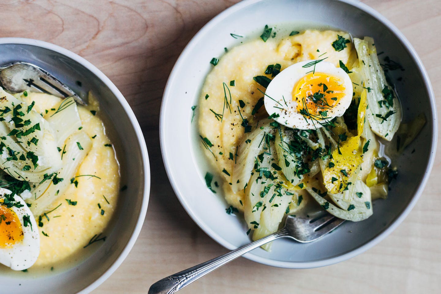 Bowls of polenta with braised fennel and leeks, a jammy egg, and herbs. 