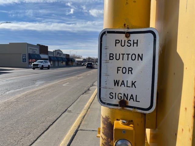 A crosswalk on main street Sioux Center, Iowa, with a "push button for walk signal" sign in the foreground