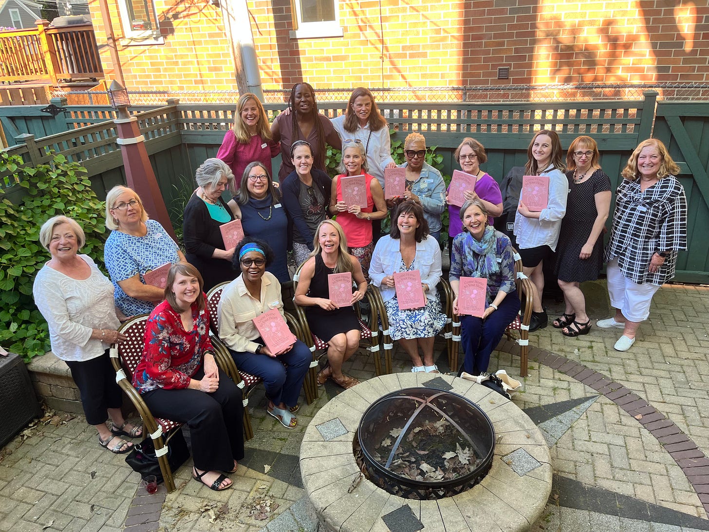 19 women gather in a backyard garden, holding books in honor of a new book release