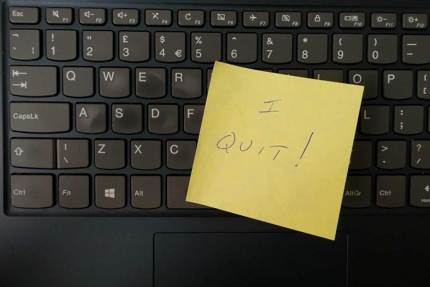 Black keyboard with yellow sticky note posted on it, reading "I quit!"