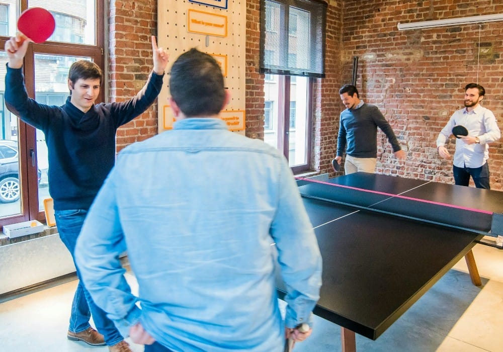 Four men playing ping pong in a red brick office workspace