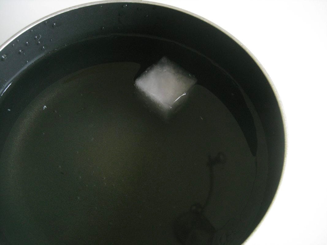 A pot of water with a cube of ice floating in it. The topmost face of the ice cube is parallel to the surface of the water.