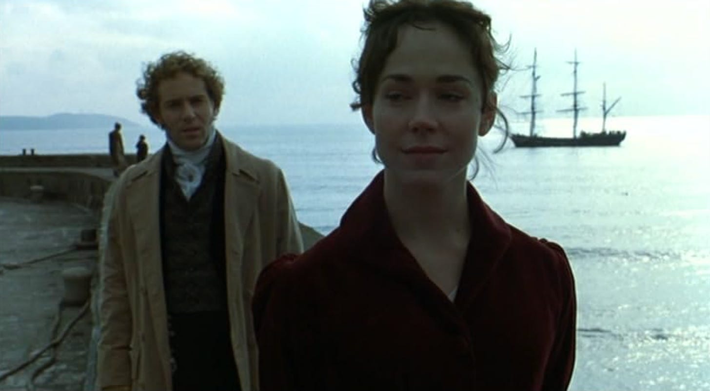 Frances O'Connor is Fanny Price, standing with her back to the sea, looking off wistfully to the side, as the actor Alessandro Nivola approaches her. They stand on a seaside cobb, under a grey English sky. The still is from Paticia Rozema's 1999 production of 'Mansfield Park'. 