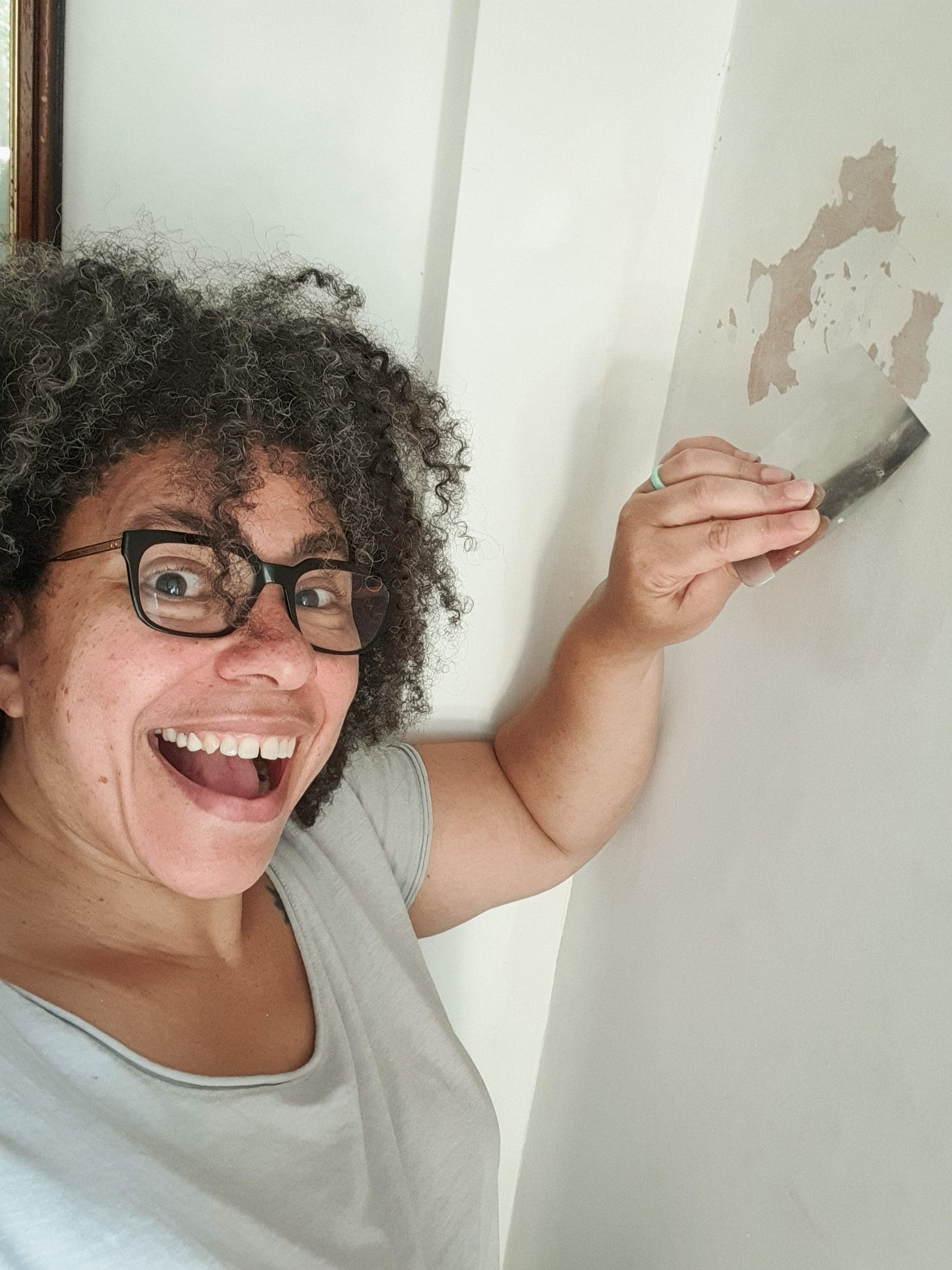 Photo of a woman scraping a wall and smiling to the camera
