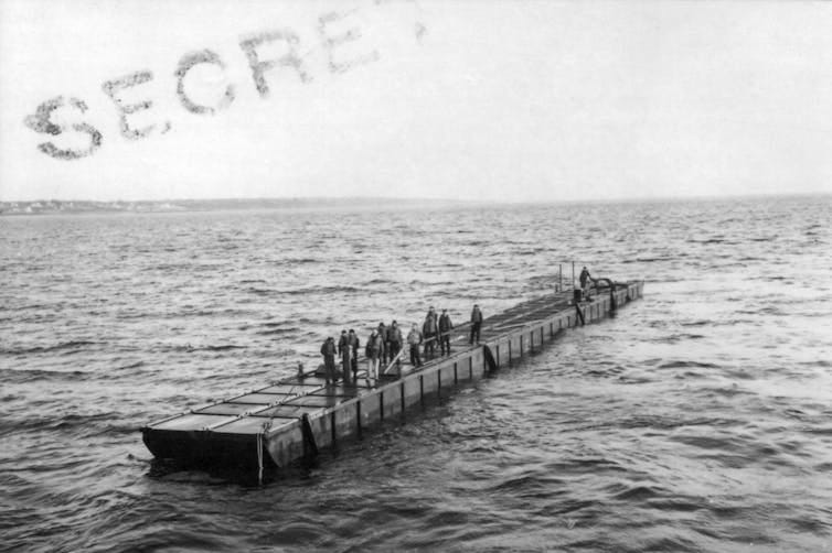 A floating platform made of boxes secured together carries people over the water.