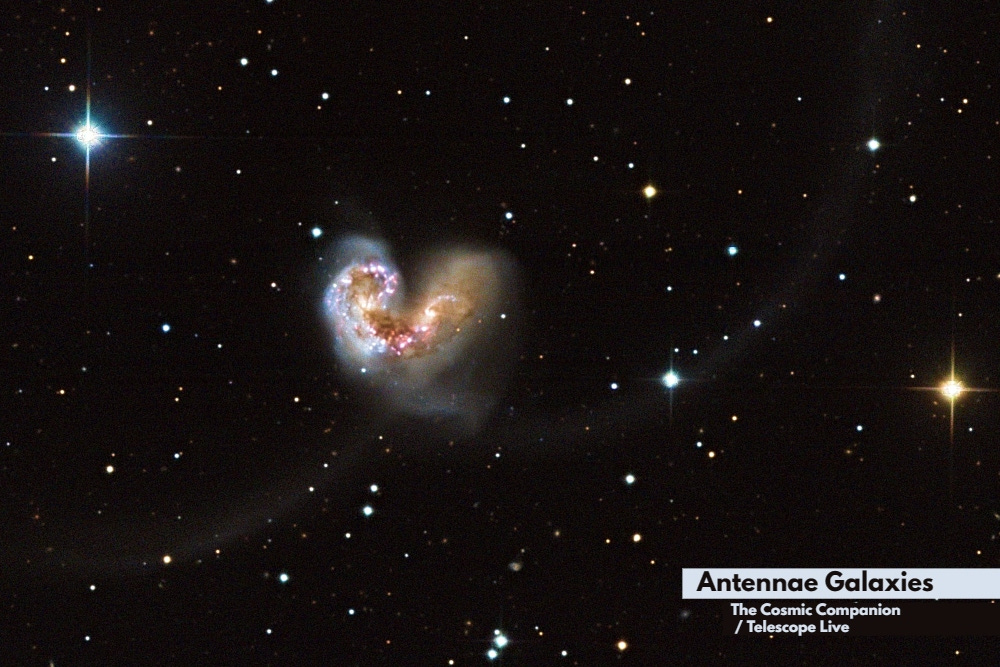 A pair of galaxies merge into a heart shape, with two long runners seen headed to the left and right sides of the image.
