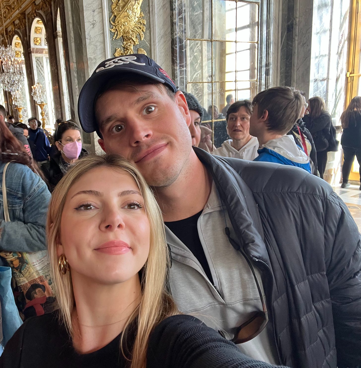 A man and woman with their heads touching, taking a selfie at the Palace of Versailles