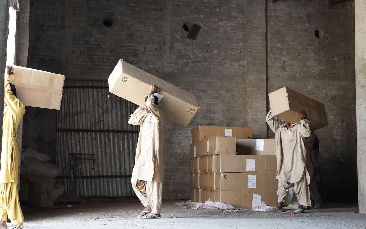 Workers carry relief material out of Oxfam TKF warehouse in dist