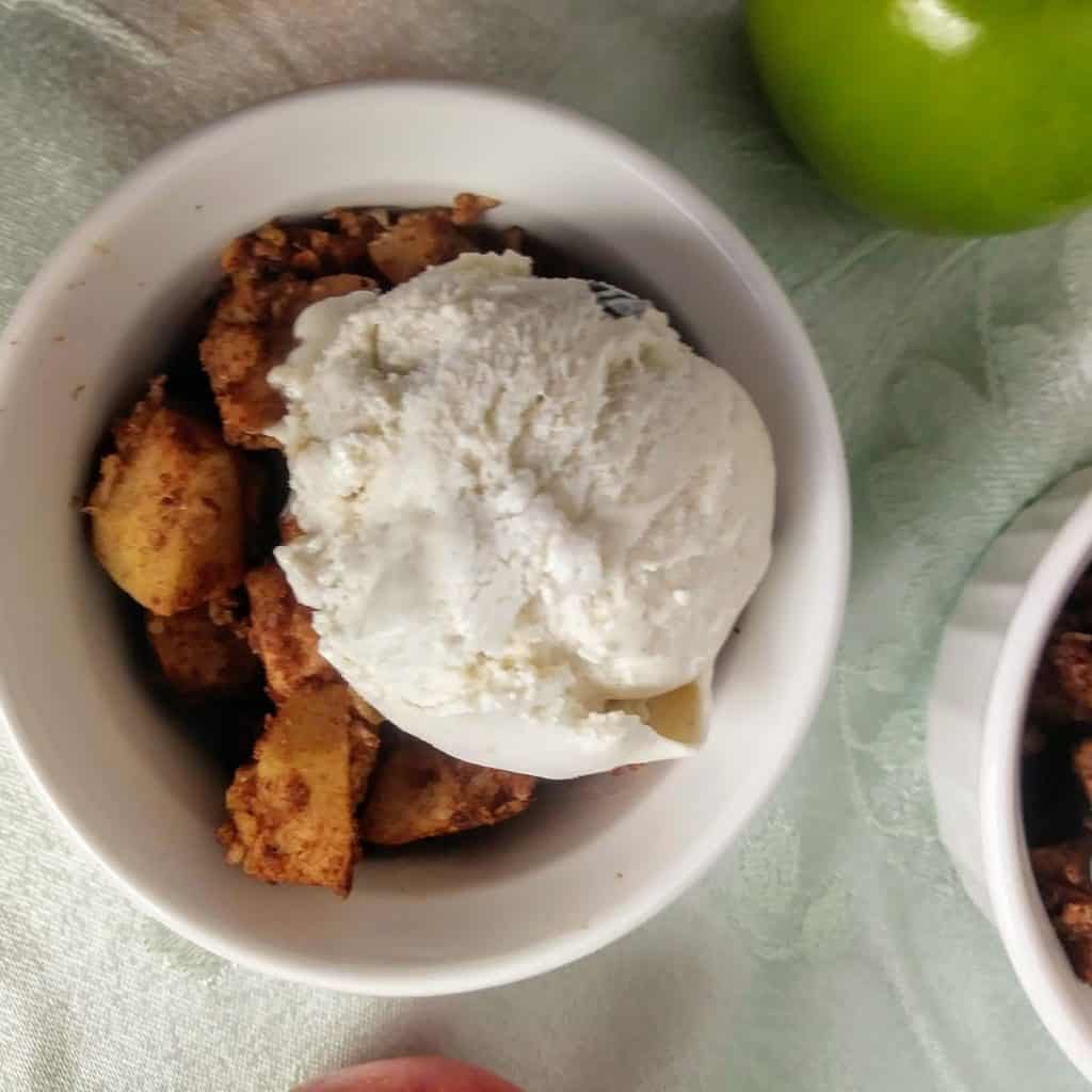 apple crisp in white bowl topped with vegan vanilla ice cream