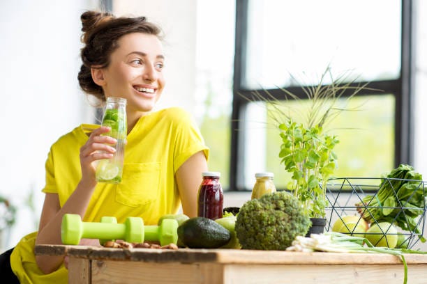 Woman with healthy food indoors Portrait of a young sports woman in yellow t-shirt sitting indoors with healthy food and dumbbells on the table detox food stock pictures, royalty-free photos & images