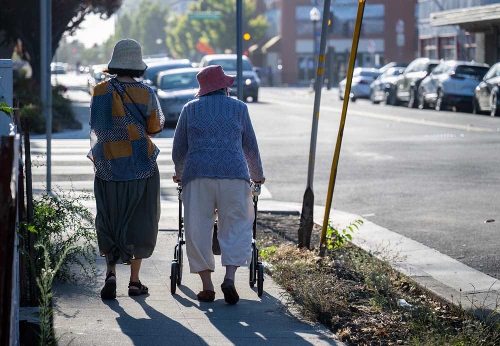 Senior woman walking using a mobility walker on the pedestrian walkway in the city, accompanied by her adult daughter.