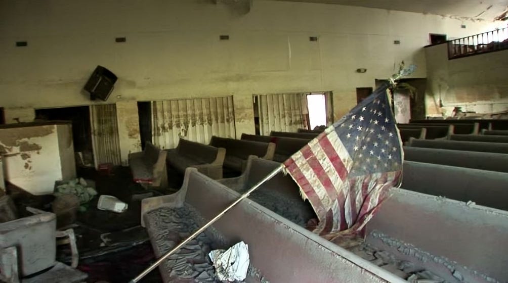 Tattered American flag in a ruined building, symbolizing America's eroding strength.