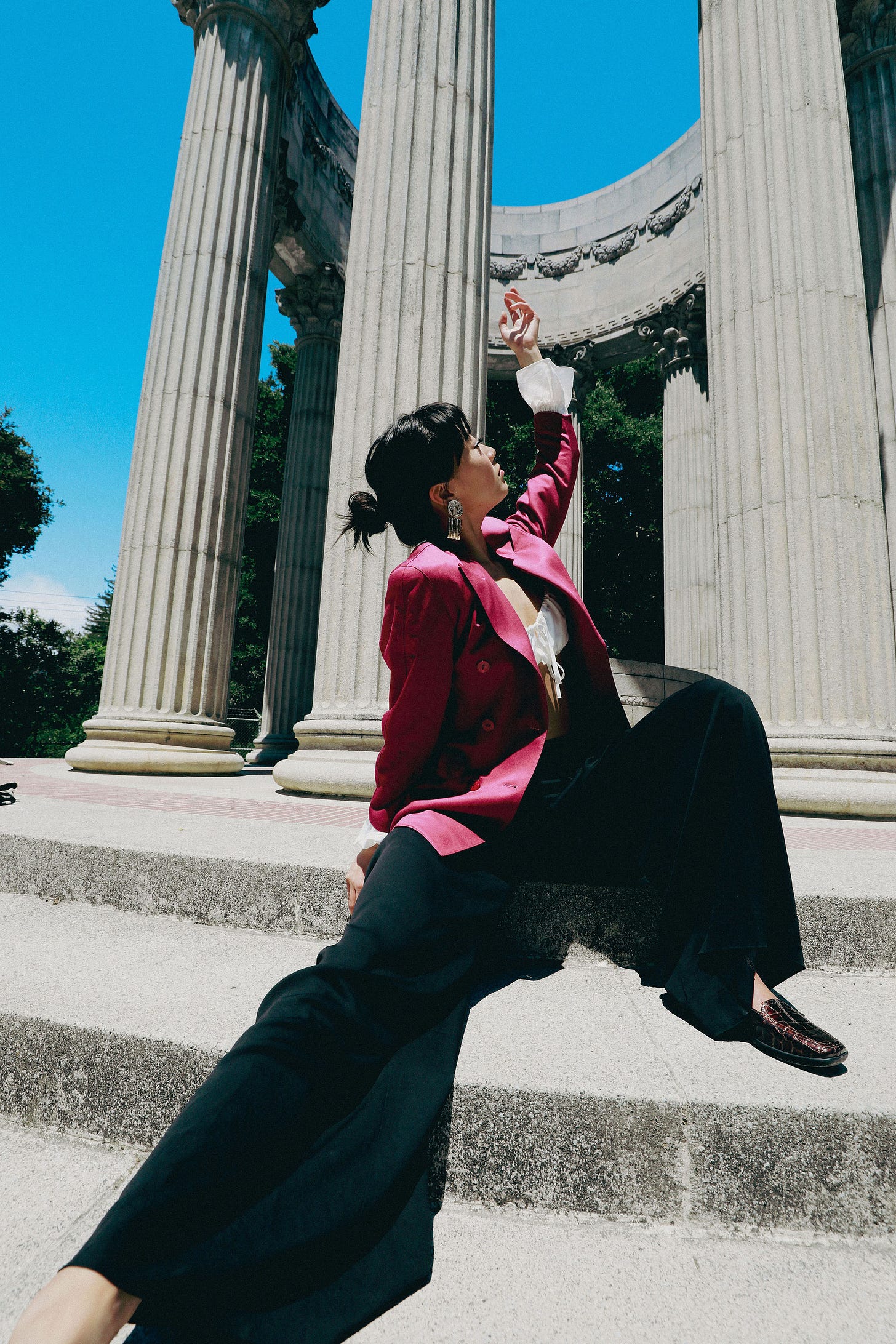 An asian woman wearing black pants and a pink blazer releasing her hand into the sky 