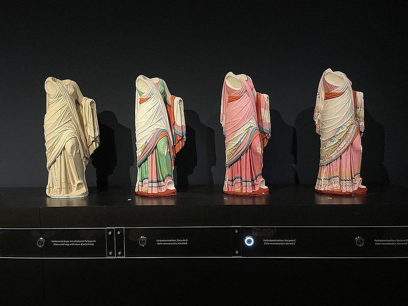 Old Greek or Roman statues from left to right with no paint to fully painted