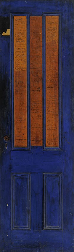Image of a thin door painted blue except for two rectangles in the middle. There are ink signatures covering it.