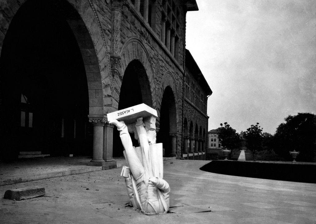 A black and white photo showing a statue of Louis Agassiz in Stanford University, which has been toppled from its mount and became wedged head-first into the ground, after the 1906 San Francisco earthquake