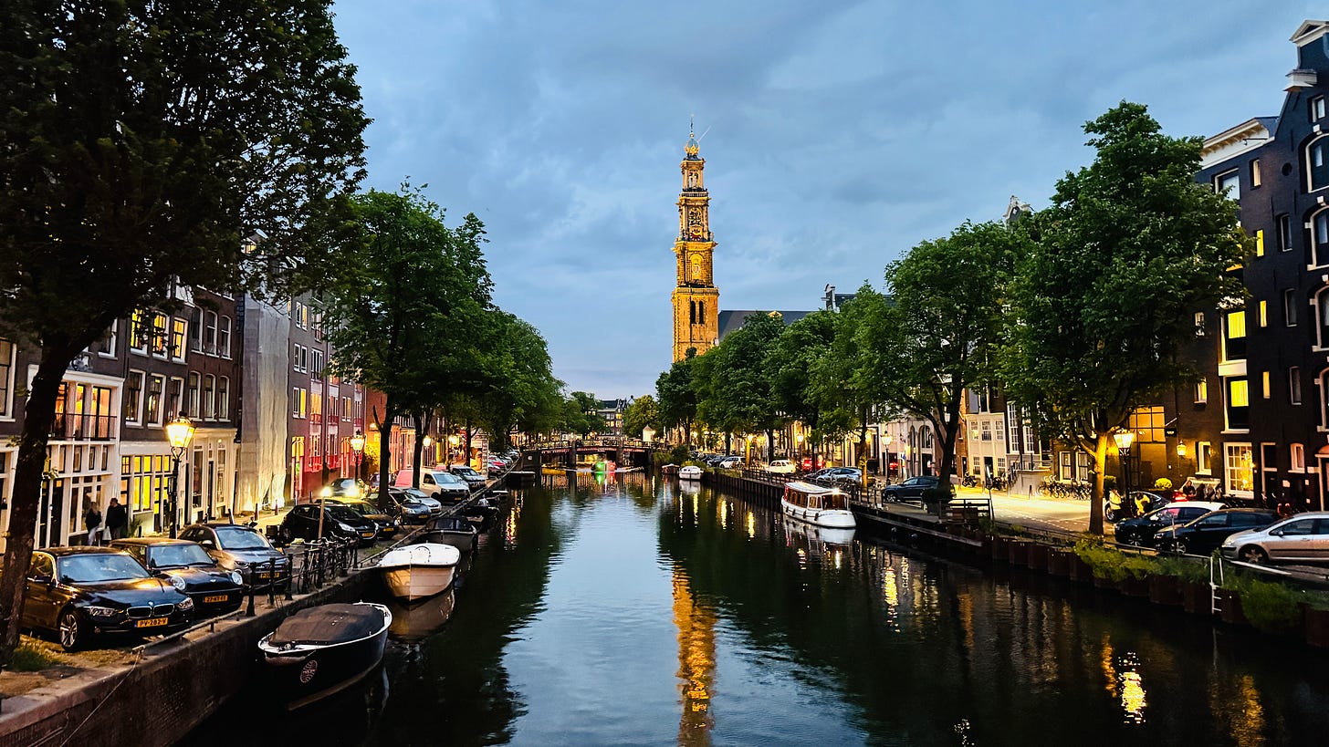 Picture of an Amsterdam canal as dusk falls. In the background looms a church spire.