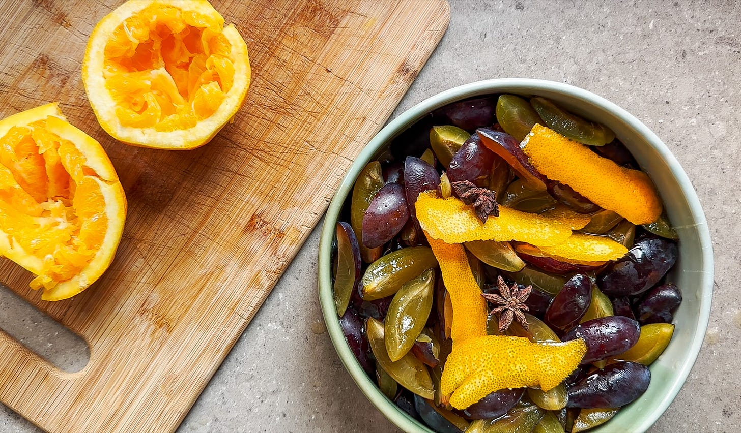 A photo of orange rinds on a cutting board and a ceramic dish of plums, honey, orange zest, and star anise.