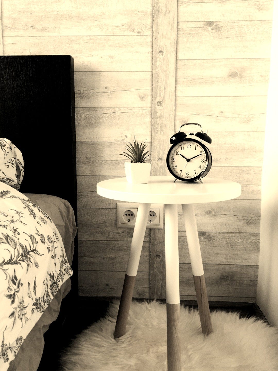 black alarm clock at 10:10 on white wooden table near table black alarm clock at 10:10 on white wooden table near table