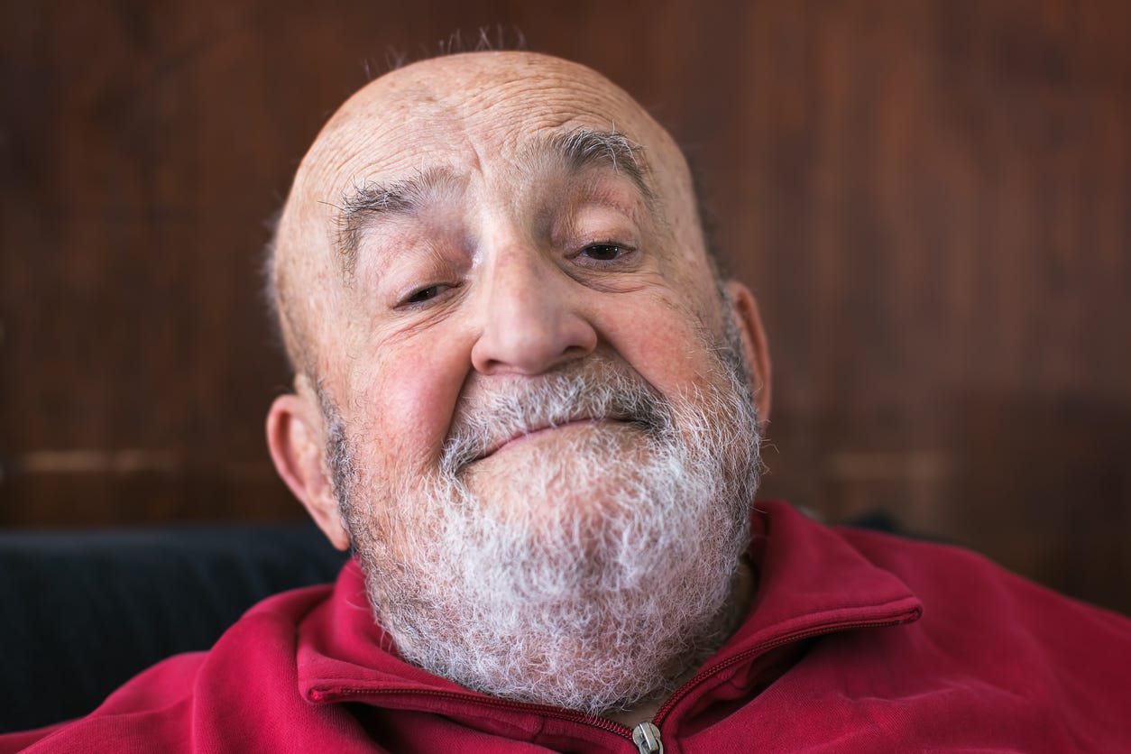 A relaxed, aging white man with a bald head and gray beard throws his head back slightly with a smile.