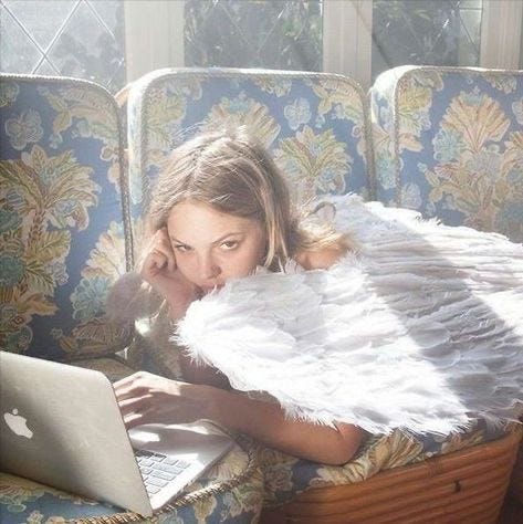 This may contain: a woman laying on a couch with an angel wings blanket over her head using a laptop