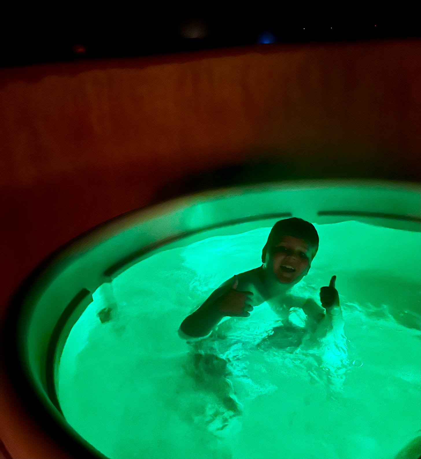 boy in neon lit hot tub at night