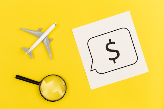 Free photo airplane model magnifier and dollar sign on yellow background flat lay