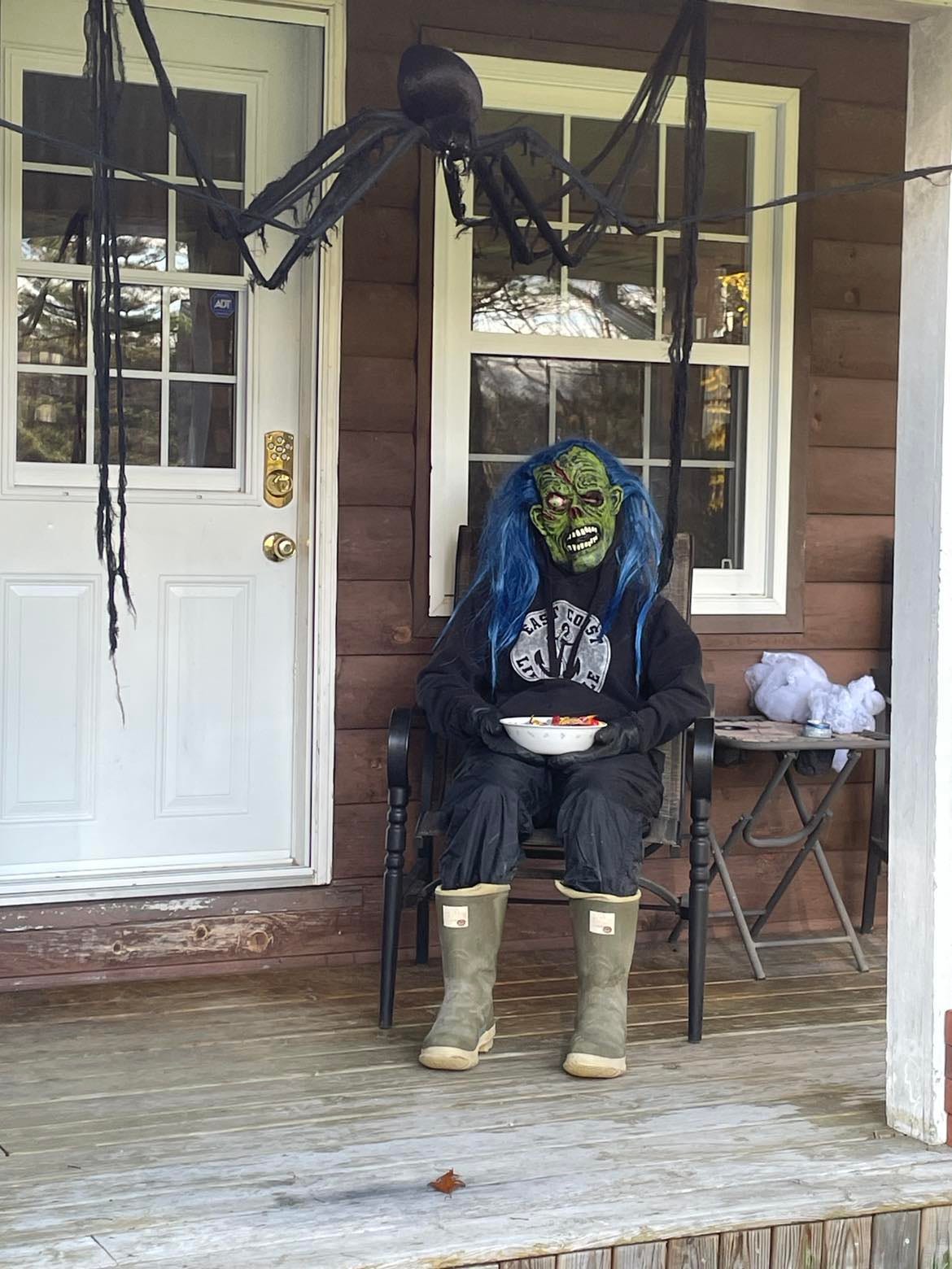 sitting on the porch holding a bowl of candy with a scary mask on.