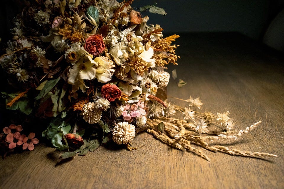 Foto de um buquê formado por diferentes tipos de flores já murchas, sobre uma superfície marrom aparentando ser madeira.