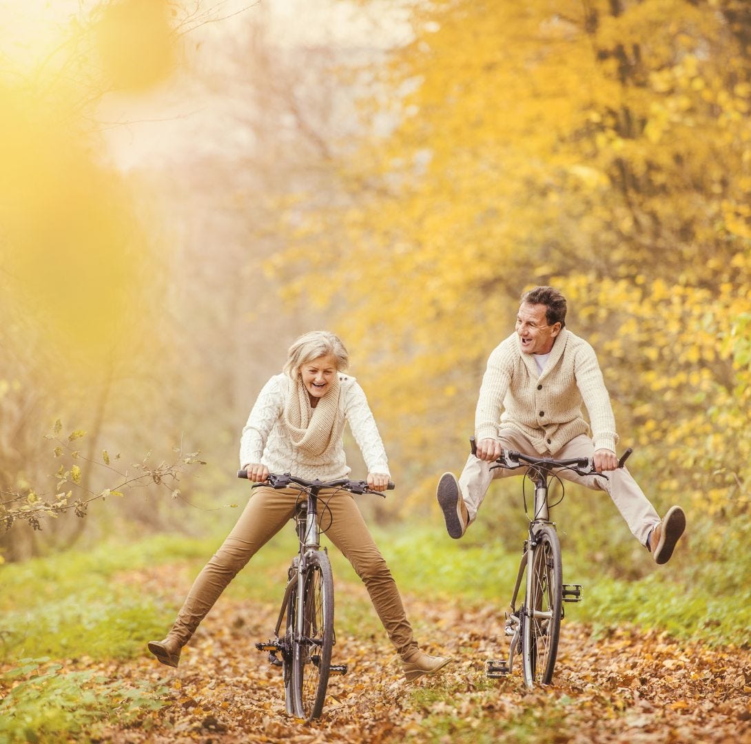 Older man and woman having fun on their bicycles in beautiful autumn scenery