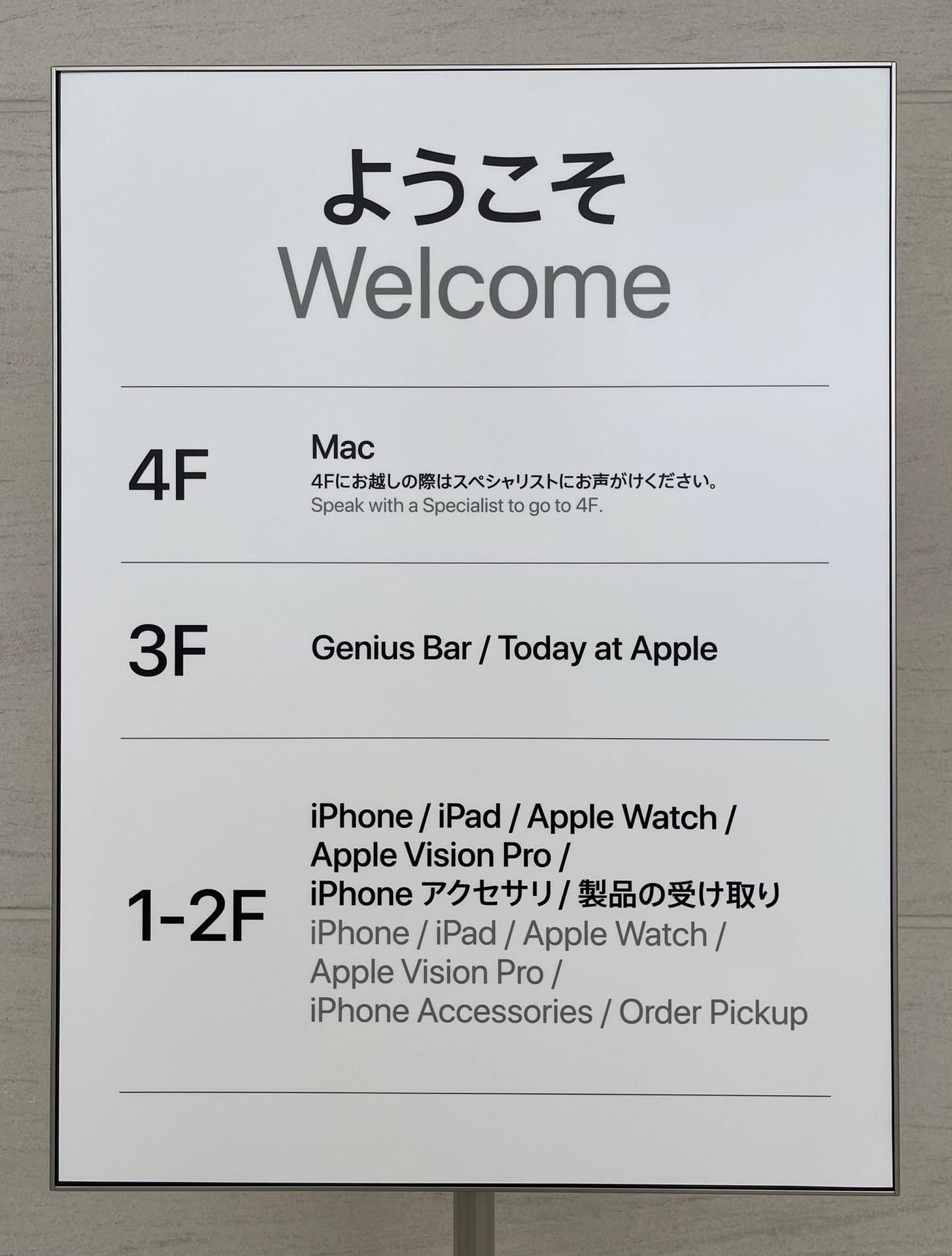 An easel inside Apple Shibuya with the floor layout listed. "Mac — Speak with a specialist to go to 4F" appears on the easel.