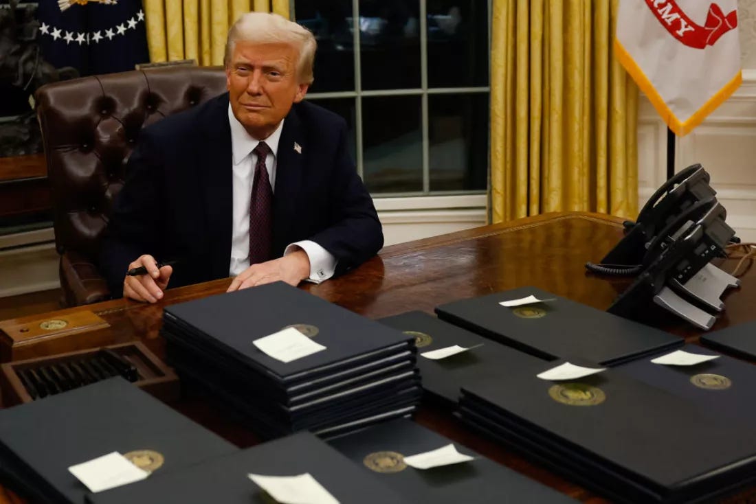 President Donald Trump in the Oval Office with stacks of black folders on his desk