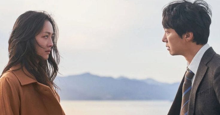 This may contain: a man and woman standing next to each other in front of the ocean with mountains behind them