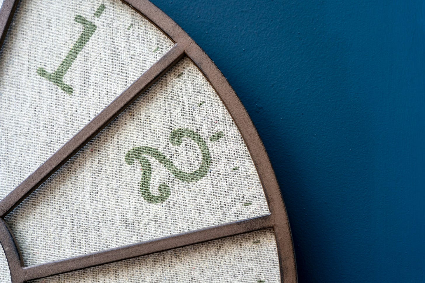 Closesup of a brown wood and beige fabric clock showing the green numbers 1 and 2, on a peacock blue background