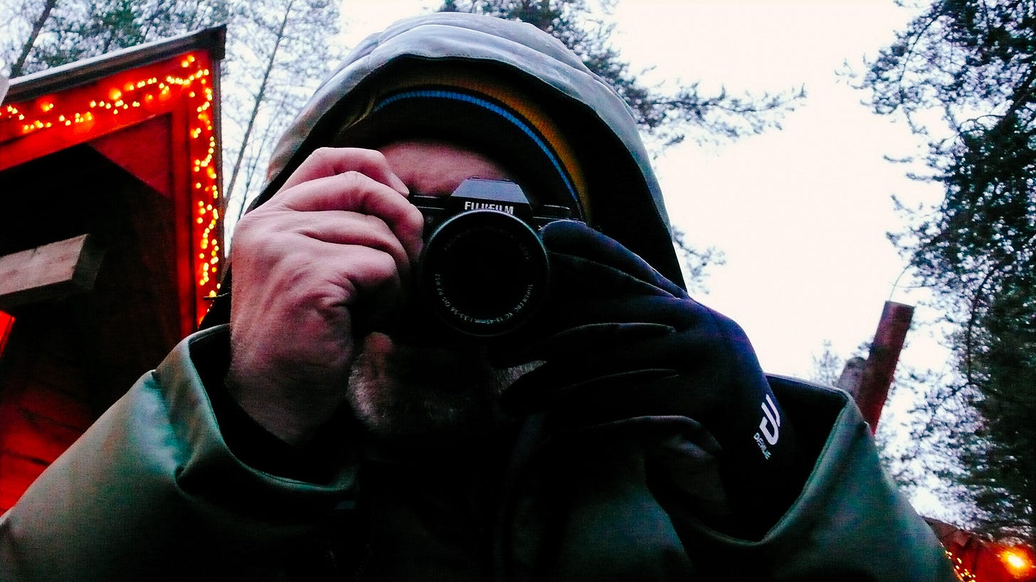 Me taking a photo of whoever is taking this photo. I'm in snow clothes and there's a Christmas decorated hut behind.