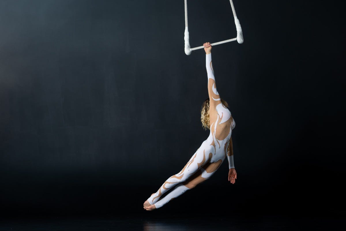 A young woman performs the acrobatic elements in the air trapeze. Studio shooting performances on a black background