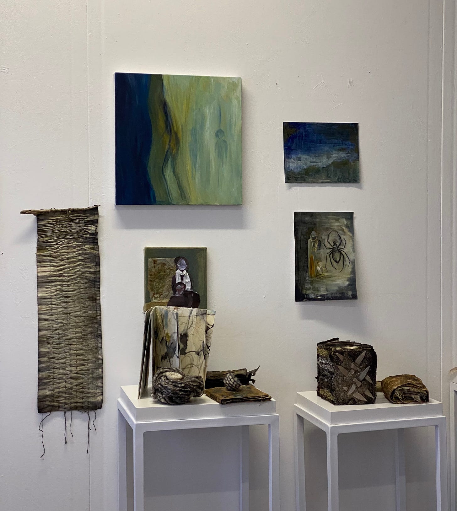 a selection of art work in shades of blues, greens and neutrals arranged on walls and two display tables