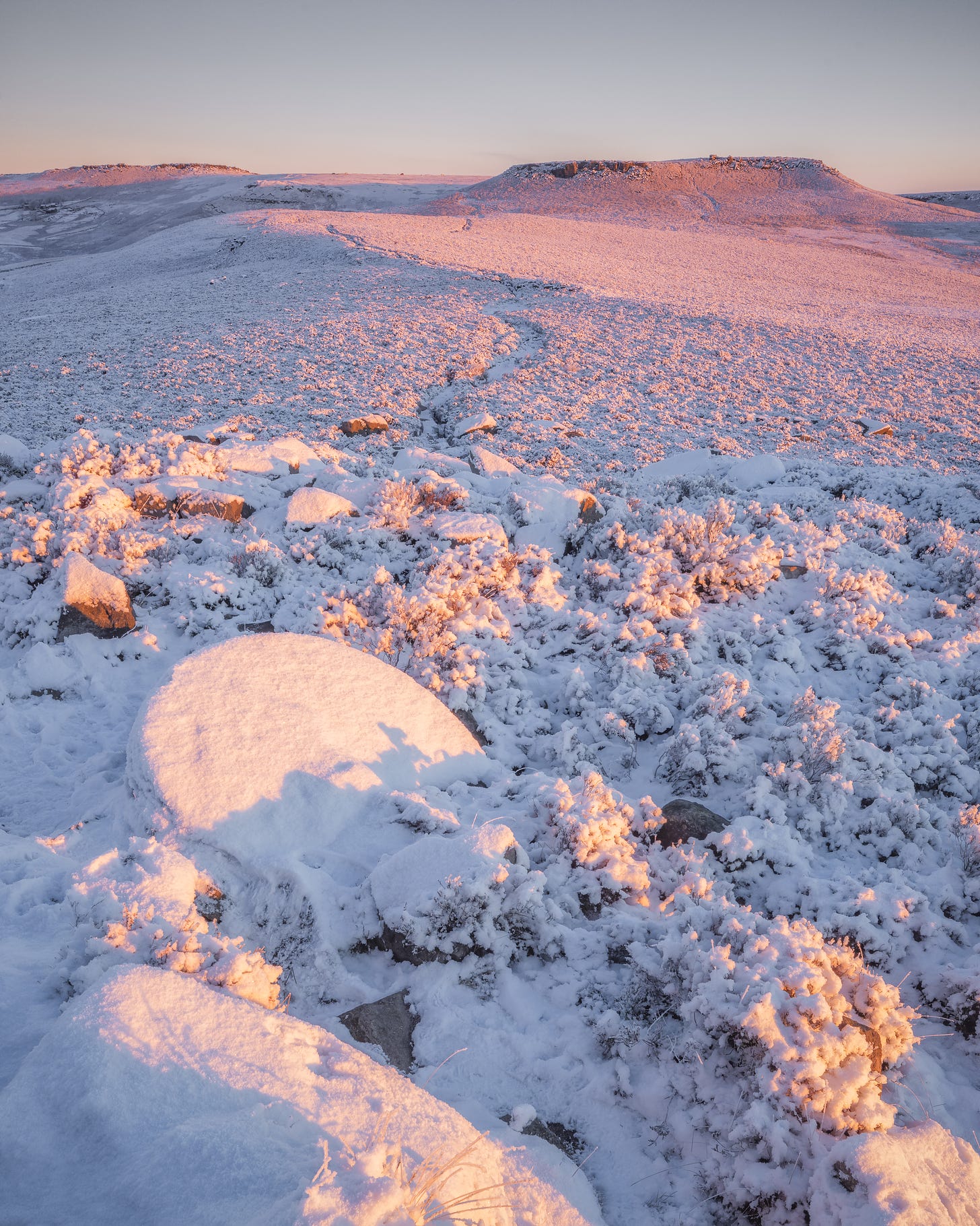 A snowy landscape from the peak district, the light of the rising sun is turning the snow pink