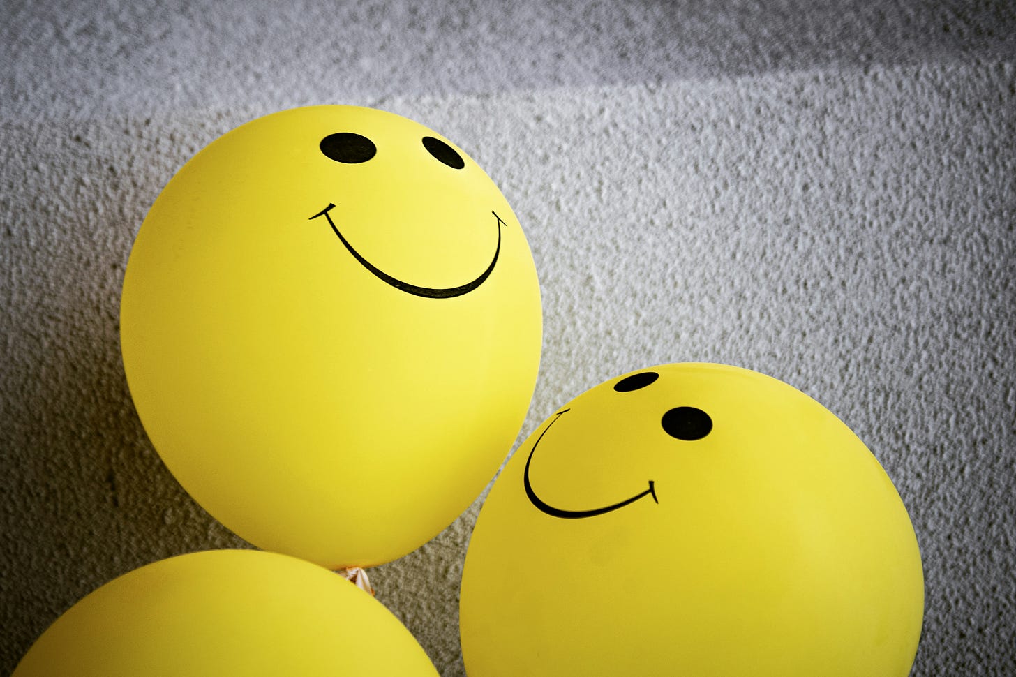 Two yellow balloons with smiley faces in black ink lying on a gray floor.