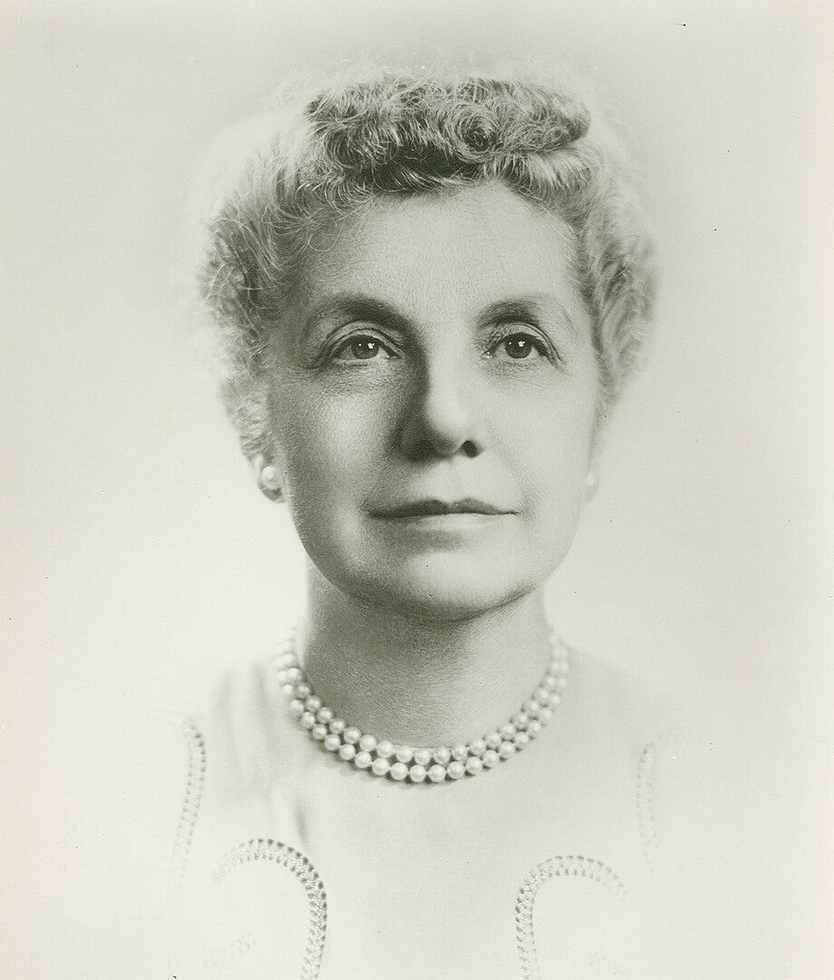 Black and white photo of woman in her 60s with short gray hair, pearls, and a cream colored dress