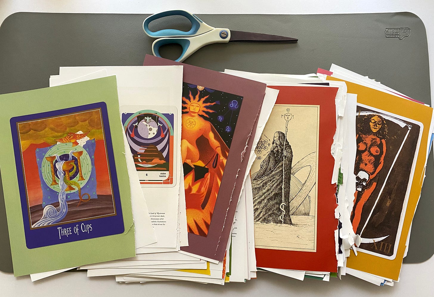 Pages from the Library of Esoterica: Tarot book that are cut out and laid on a desk under a pair of white and blue scissors. 