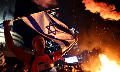 A woman waves an Israeli flag near a bonfire.