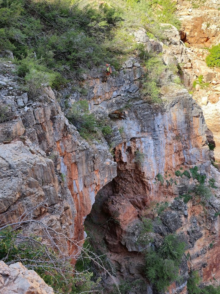 Someone rappelling over a cliff into a large cave entrance in the cliff